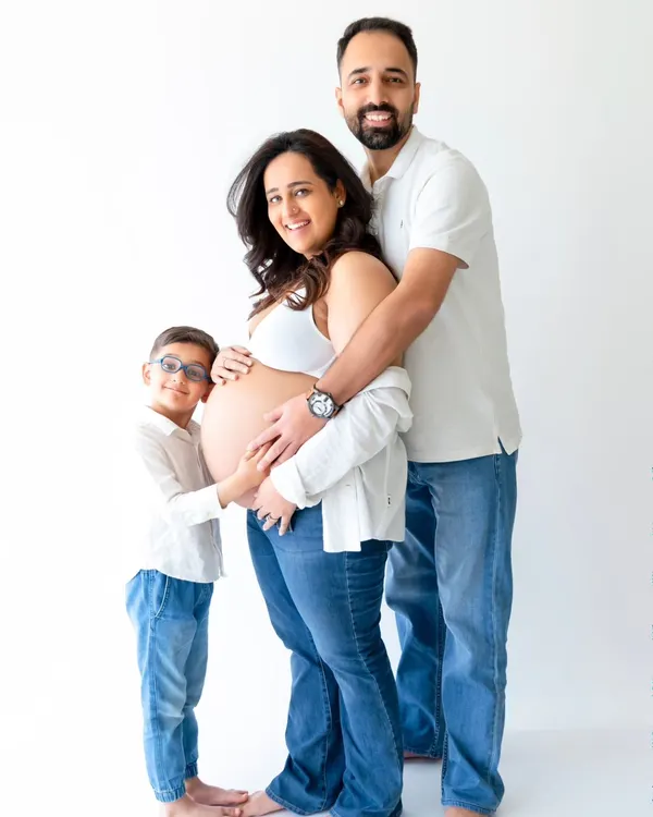 A heartwarming family maternity photo where an older sibling joins his parents to embrace the baby bump. This shot captures the excitement of the entire family in a clean, modern studio style.