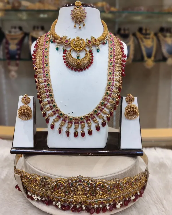 A classic kempu stone bridal set with a crescent-shaped pendant, paired with a matching long haram, jhumkas, and an intricate hip belt.