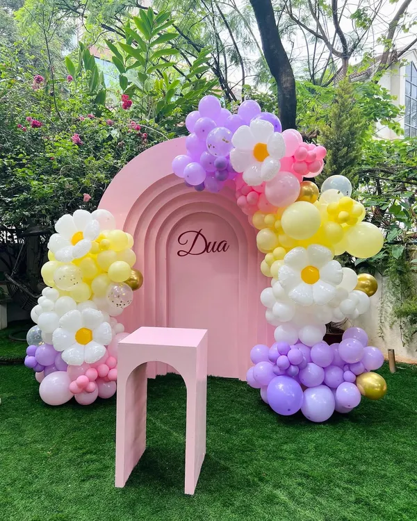 A pretty garden setup for Dua's first birthday, featuring a pink arched backdrop with her name. The daisy-shaped balloon clusters add a whimsical and charming touch to the outdoor decor.
