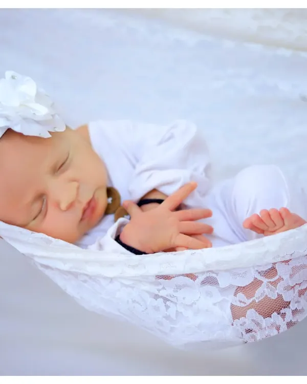 A peaceful newborn sleeps soundly in a white lace hammock against a clean white background. This style of portraiture emphasizes the baby's innocence and tranquility.