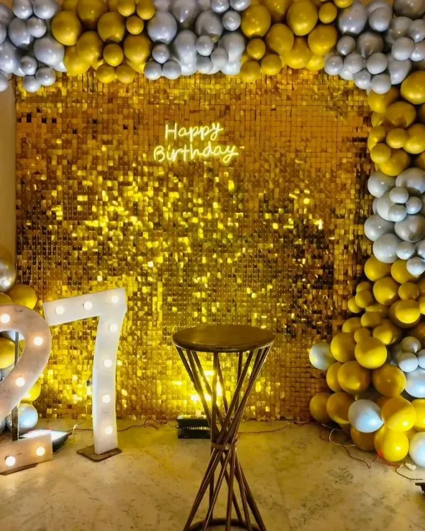 A dazzling gold sequin wall makes a statement at this 27th birthday party. Framed with gold and silver balloons and paired with marquee numbers, it creates a truly glamorous focal point.