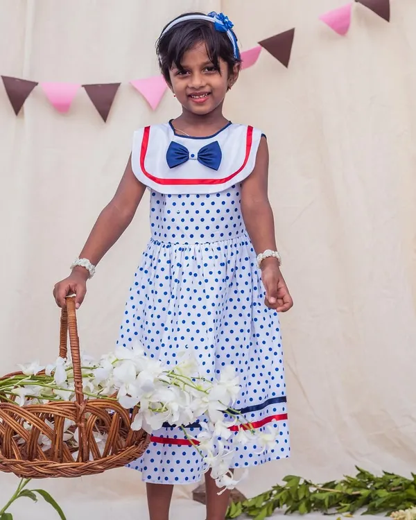 A classic look for a sunny day. This white and blue polka dot dress with a sailor collar is perfect for a picnic or a stroll, and she looks adorable holding a basket of flowers.