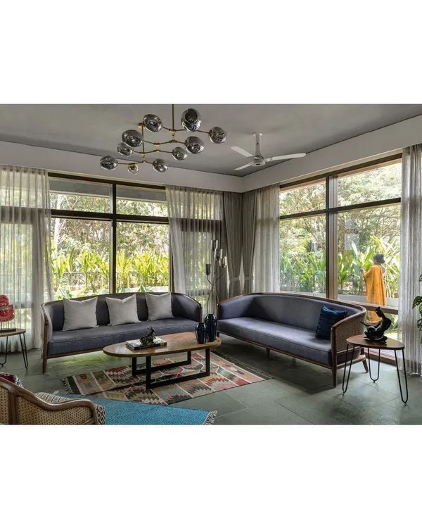 A living room set featuring two custom sofas with exposed wood frames and cane paneling. The design is complemented by a low-profile oval coffee table and hairpin leg side tables, creating a balanced composition of modern and natural materials.