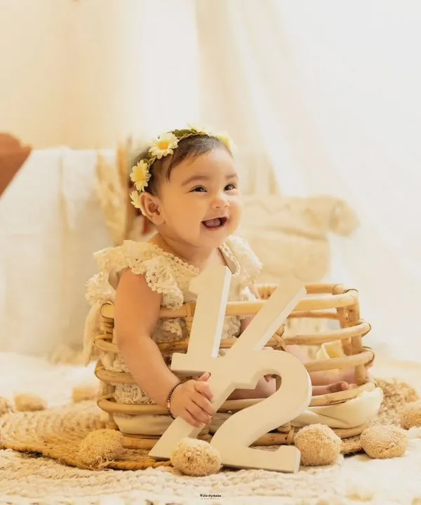 Celebrating six months. This happy baby girl marks her half-birthday with a '1/2' sign in a beautiful, bohemian-style studio setup.