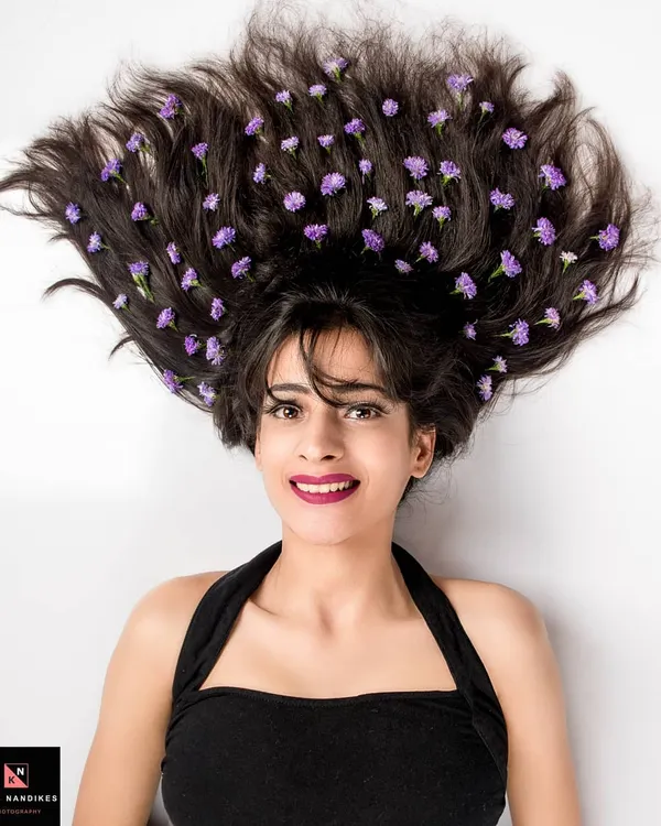 A creative overhead portrait with the model's hair spread out and adorned with small purple flowers. Her expressive face and the unique styling make this a standout artistic shot.