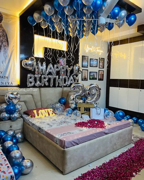 An elaborate and romantic 29th birthday room decoration. The setup includes balloons on the ceiling, 'Happy Birthday' and number foils, a 'LOVE' marquee light, and a rose petal pathway.
