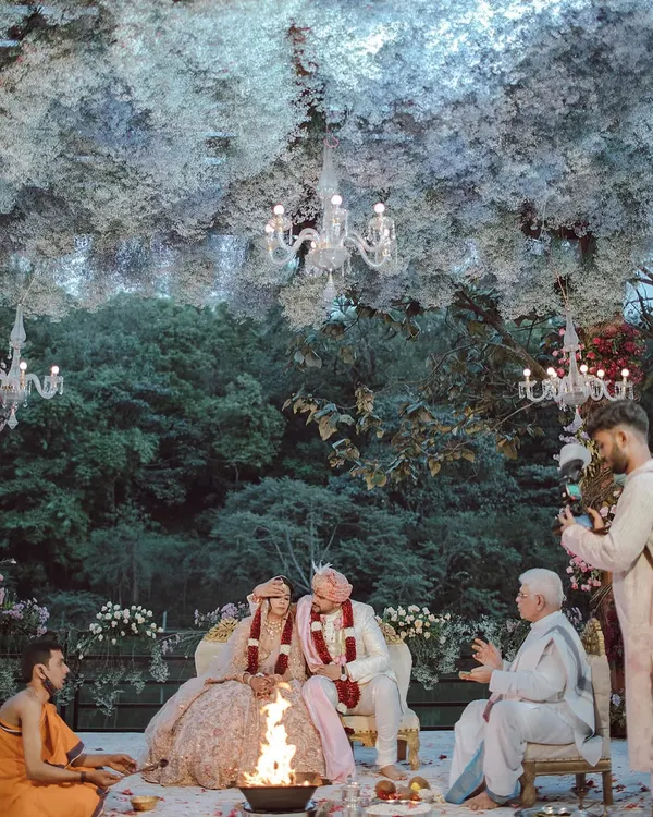 A couple shares a smile during their ceremony, seated under a magical ceiling of white flowers that feels like a cloud. We designed this space to feel like an enchanted forest, creating a warm and beautiful setting for their union.
