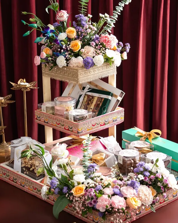 A magnificent three-tiered festive hamper, overflowing with an assortment of gourmet treats and adorned with lush, vibrant floral arrangements. This is the pinnacle of luxury gifting, perfect for making a grand statement during celebrations like Diwali.