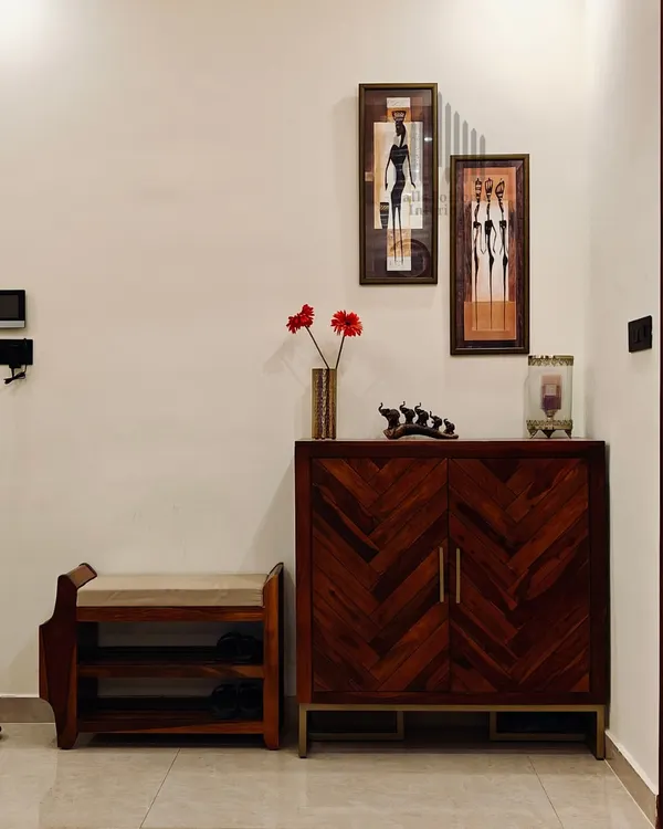 A warm and welcoming foyer featuring a chevron-patterned wooden shoe cabinet and a matching bench, complemented by ethnic art pieces.