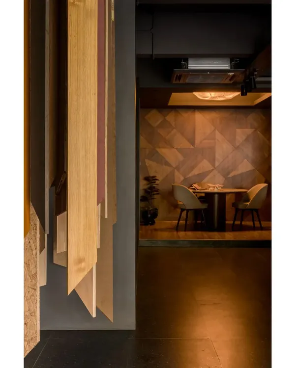 A view into a private discussion nook within the veneer showroom. The wall is clad in a geometric veneer pattern, creating a sophisticated and moody atmosphere for client meetings.
