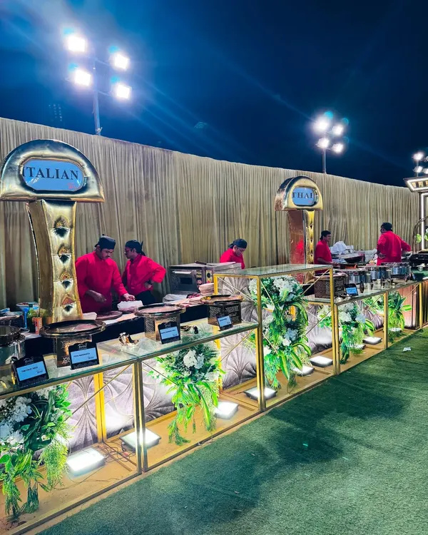 An overview of our elegant Italian food counter at an outdoor evening event. The setup features gold and white decor, beautiful floral arrangements, and dedicated chefs ready to serve fresh pasta and other Italian specialties.