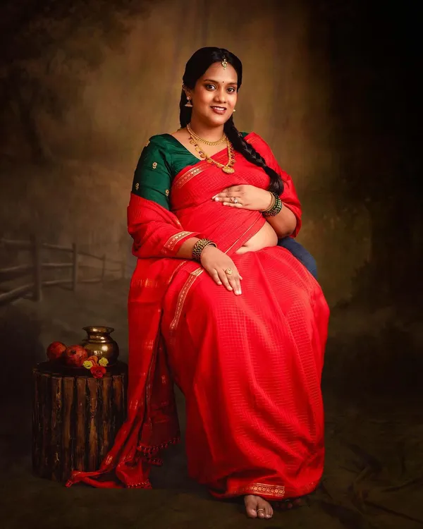 A classic portrait celebrating motherhood in a beautiful red saree. The painted backdrop and traditional props in my studio help create a timeless, regal look.