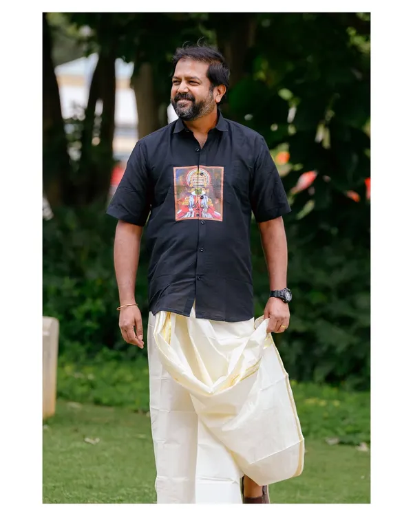A candid-style shot of the model in a custom-printed black shirt and traditional mundu. This image captures a natural, relaxed moment, perfect for lifestyle branding.