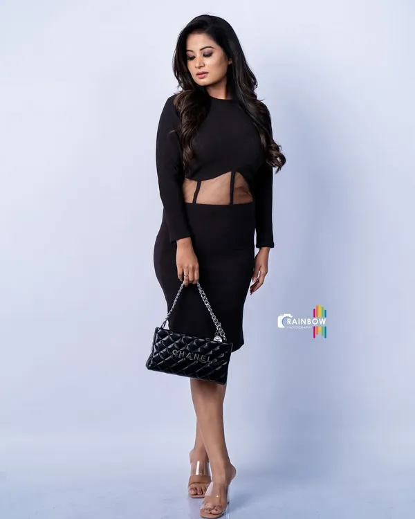 A full-length studio shot of a model in a sleek black dress. The clean white background and sharp lighting create a high-fashion look that emphasizes the model's pose and the outfit's silhouette.