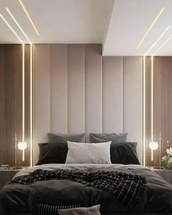 A luxurious bedroom concept featuring a floor-to-ceiling upholstered headboard flanked by wood panels. Integrated vertical lights and modern bedside lamps create a warm and inviting ambiance.