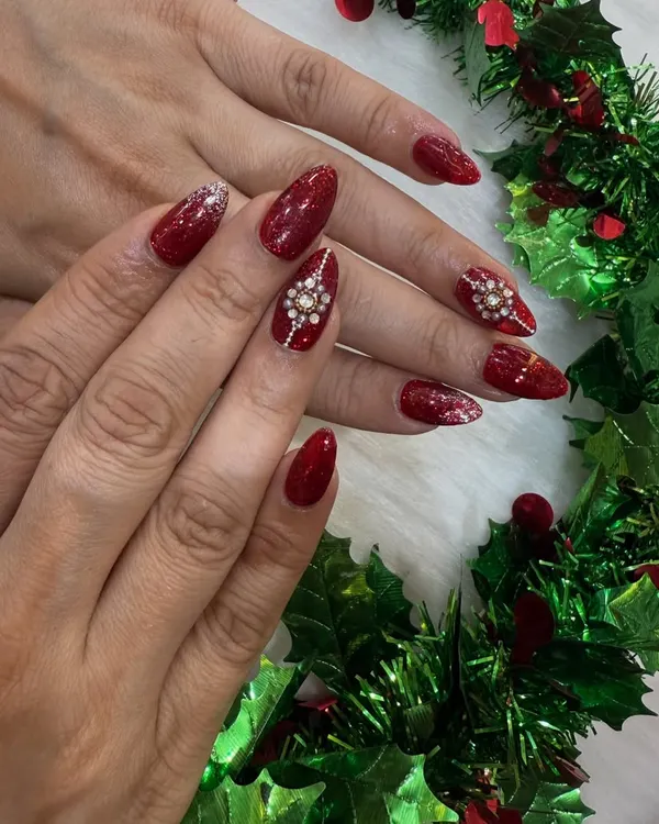 The ultimate Christmas party nails. This look features a rich, sparkly red base on almond nails, with two accent nails adorned with stunning, hand-placed diamond snowflake designs.