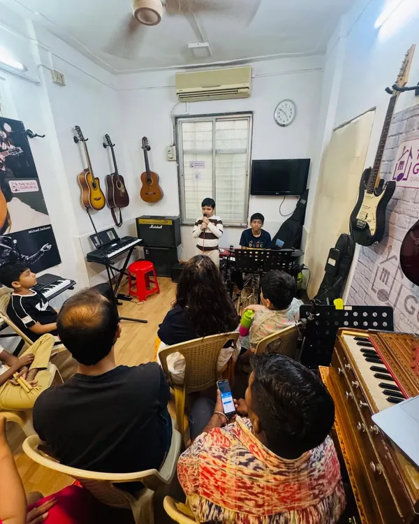 A wide shot of our 'Musical Saturday' jam session. An audience of parents and fellow students watches attentively as a young performer takes the stage, creating a real concert atmosphere.