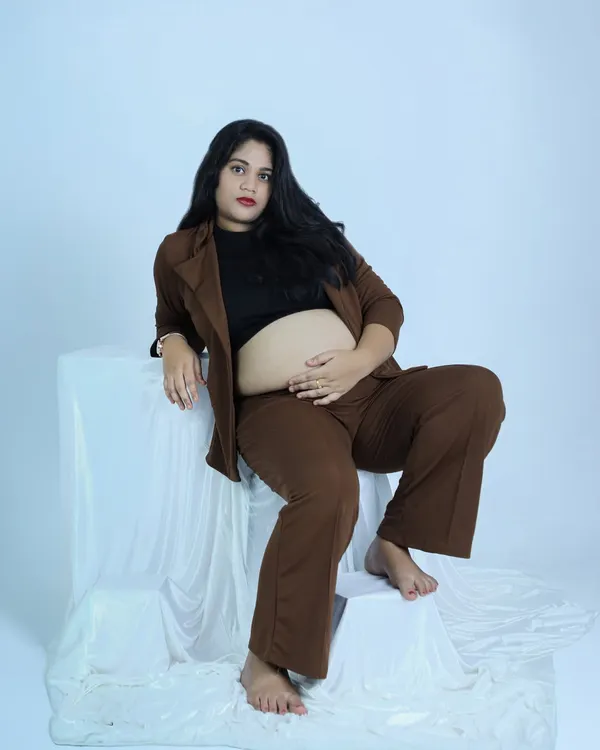 A modern and confident maternity portrait. The mother-to-be wears a stylish brown suit, showcasing her baby bump with a powerful and chic pose in our studio.