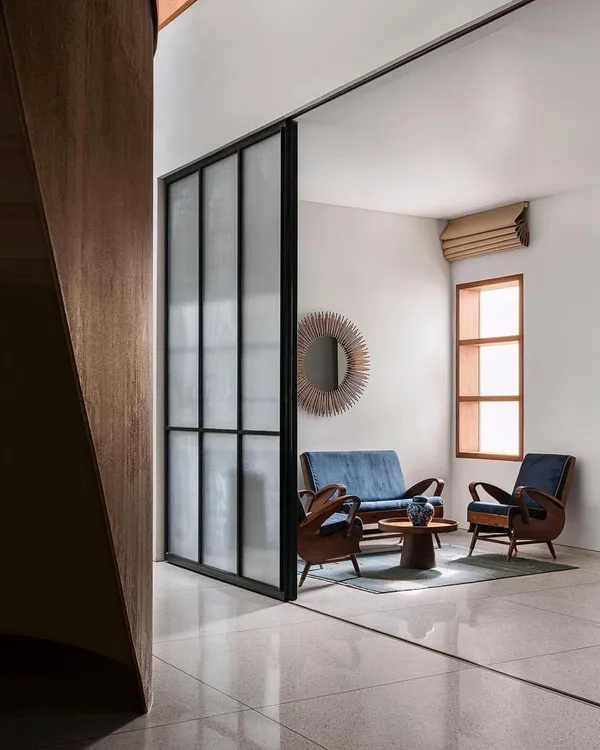 A view into a serene sitting area in the Abhikram residence, where a large sliding glass partition allows for flexible separation of space while maintaining a visual connection to the rest of the home.