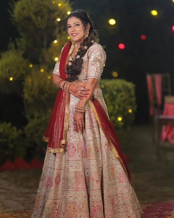 A radiant bride in her custom-made wedding lehenga. The combination of a cream base with intricate pink and red embroidery, paired with a classic red dupatta, creates a timeless and elegant bridal look.