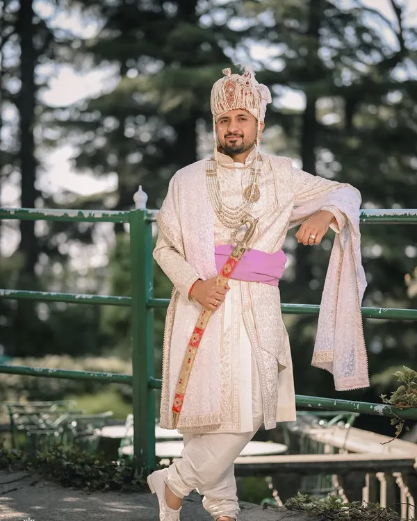A royal portrait of the groom in his white sherwani, holding a traditional sword. This shot, taken outdoors in Shimla, is full of regal charm.