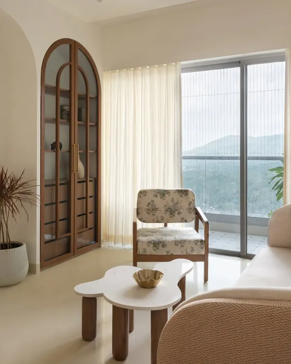 This living area is defined by its serene atmosphere and connection to the outdoors. We used a palette of soft whites and beiges, with an arched wooden cabinet and a floral print armchair adding subtle, timeless charm.