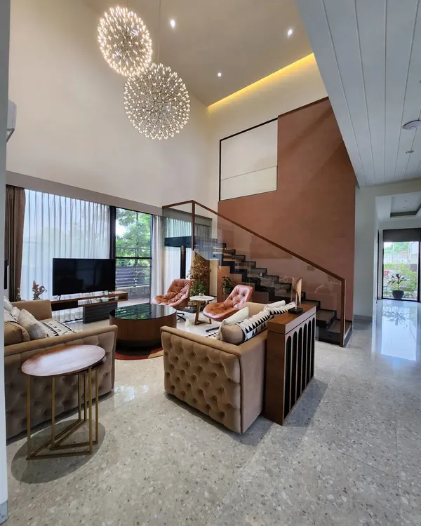 We designed this double-height living room to feel like a private resort, using expansive windows and grand chandeliers to create a sense of scale and tranquility. The space is anchored by a terracotta-colored feature wall and a modern staircase, blending warmth with contemporary design.