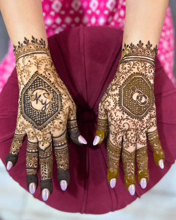 A personalized engagement mehendi featuring the couple's initials 'KY' on one hand and a motif of interlocking wedding rings on the other.