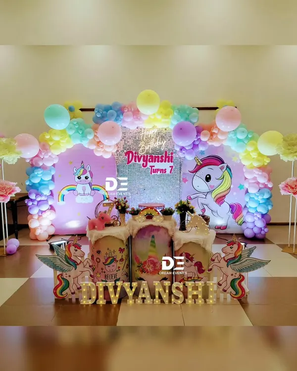 A magical unicorn fantasy for Divyanshi's 7th birthday. This setup features a sparkling backdrop, a rainbow of pastel balloons, and adorable unicorn cutouts, creating a truly dreamy atmosphere.