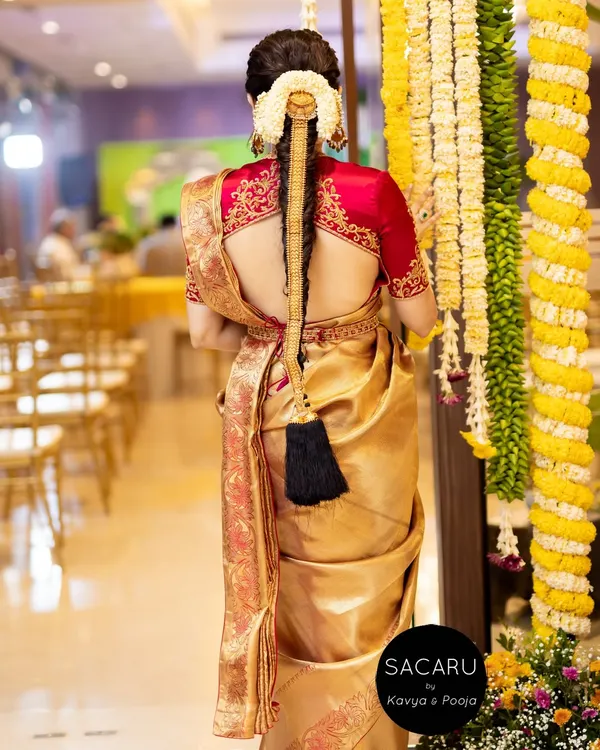 The back view of our client Anusha's bridal look, showcasing the deep back of the cherry red satin blouse and her traditional braided hairstyle.