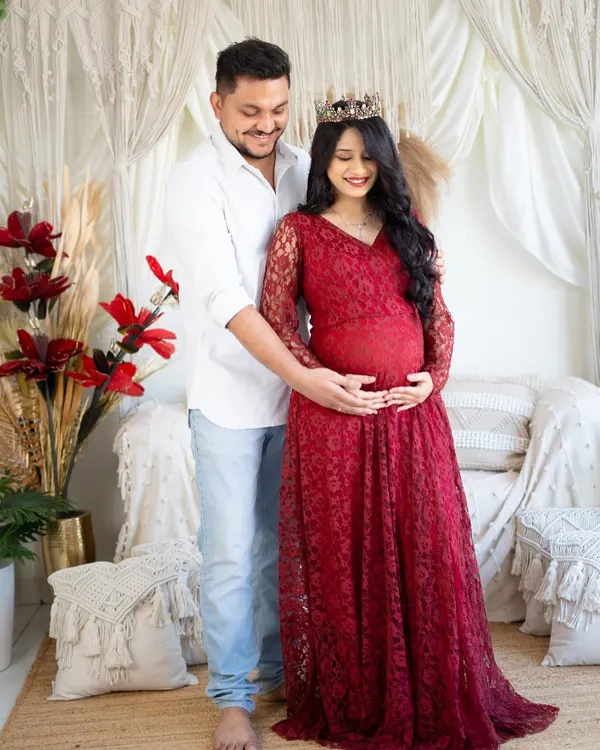 An intimate moment between partners in our boho-chic studio. The mom-to-be wears a beautiful red lace gown while her partner gently holds her, both focused on the baby bump.