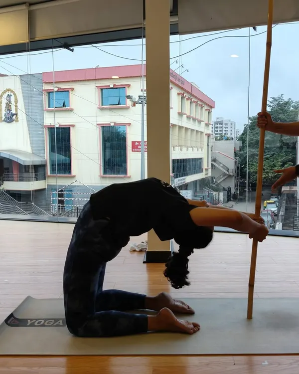 A student uses a stick for support to deepen her Ustrasana (Camel Pose), allowing for a safer and more effective backbend.