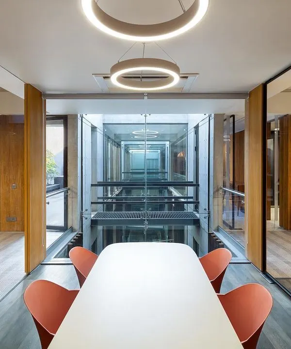 The interior planning of the Laxcon office creates visual porosity. A conference room is positioned to overlook the central triple-height void, maintaining a feeling of connection between different functional zones within the corporate building.