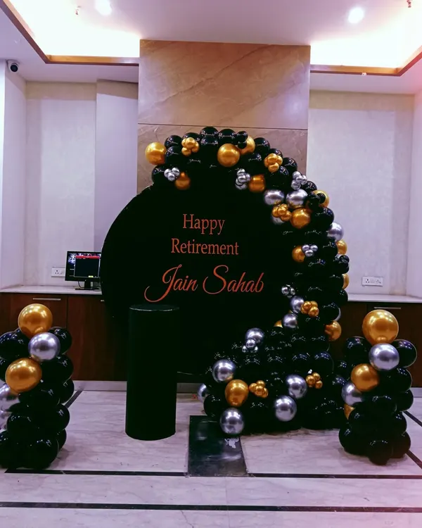 A classy retirement party setup with a black, gold, and silver balloon arrangement around a personalized "Happy Retirement" backdrop.