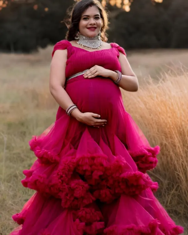 A bright pink ruffled gown stands out beautifully against a natural, grassy background. The layered tulle skirt adds wonderful texture and dimension to this outdoor maternity photo.