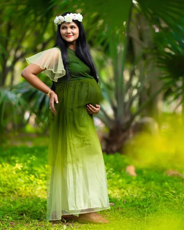 A serene moment in nature. This mom-to-be, wearing a green ombre gown and a floral wreath, looks peaceful and beautiful surrounded by lush greenery.