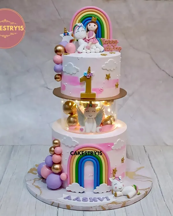 A magical two-tier unicorn cake designed for a first birthday. This choco-vanilla creation features a glowing LED-lit spacer, a fondant unicorn with wings, and charming rainbow decorations.