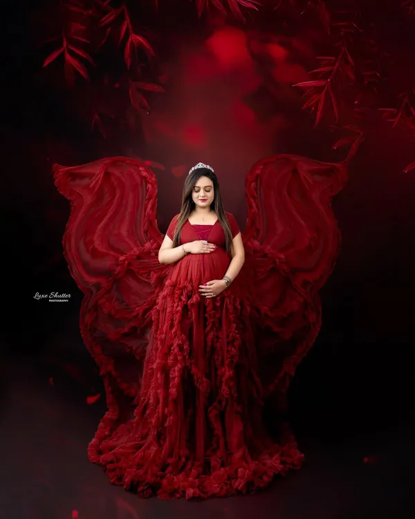 A truly magical portrait of motherhood. This mom-to-be looks like an angel in a deep red ruffled gown, with fabric wings that create a sense of fantasy and wonder.