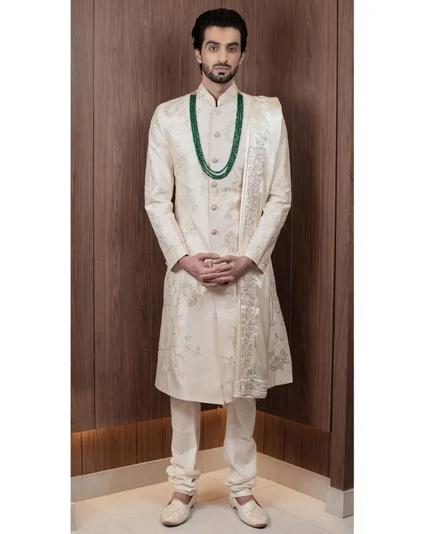 A full view of our ivory sherwani, showcasing its majestic length and the exquisite, subtle embroidery that covers the piece. Paired with a matching stole, it creates a look of pure elegance for a groom.