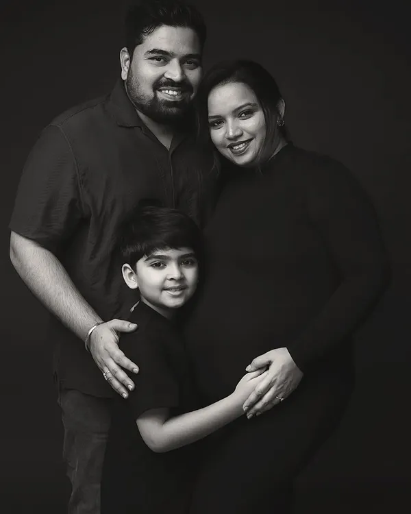 A classic black and white maternity portrait of a family of three, soon to be four. The dark background puts all the focus on their expressions of love and anticipation.