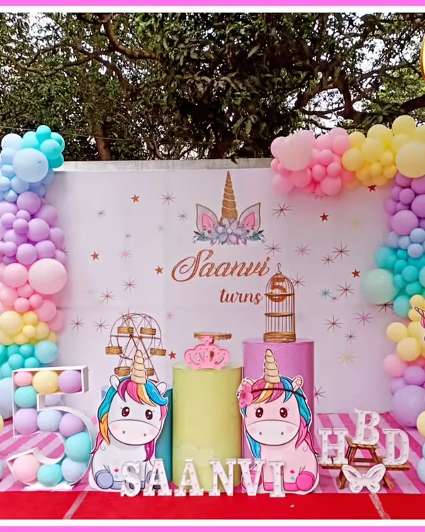 A dreamy unicorn-themed fifth birthday party. This outdoor setup features pastel balloon columns, unicorn cutouts, and a 'SAANVI' marquee.