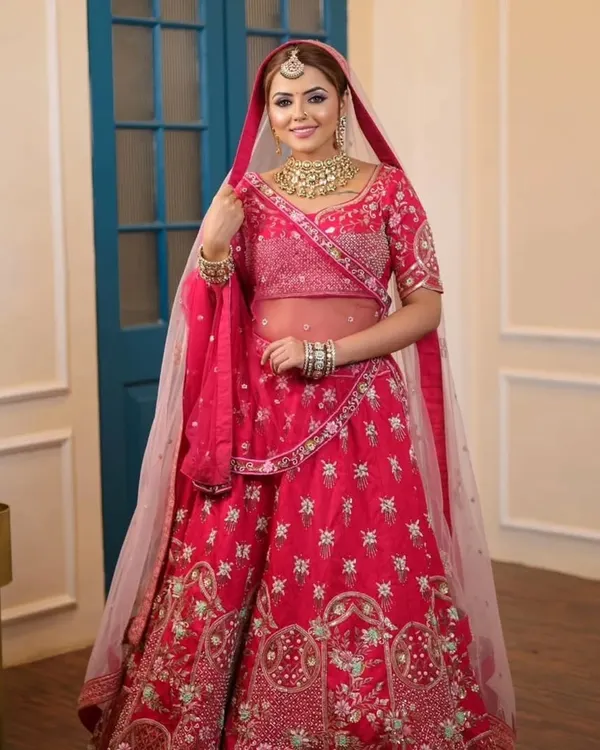 A full-length view of a classic bridal look, featuring a vibrant pink lehenga paired with a gold Kundan choker set. This is a timeless choice for any bride on her wedding day.