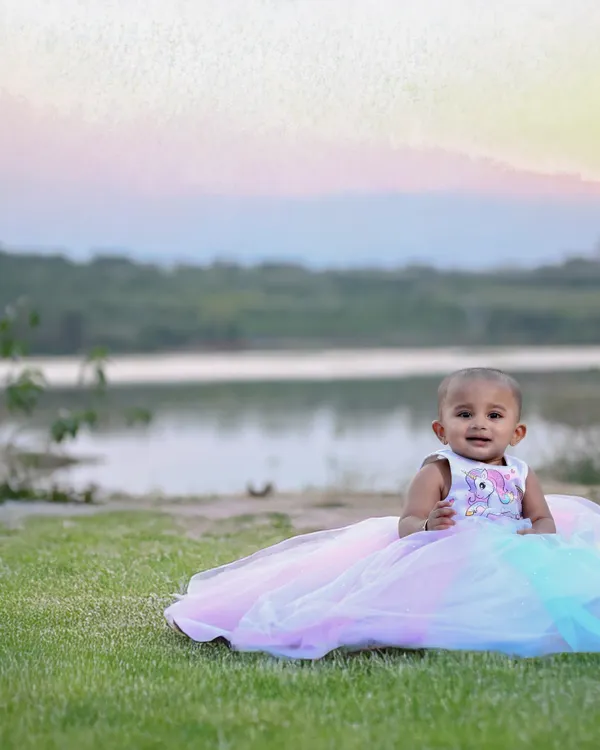 A beautiful outdoor portrait of a baby girl in a princess dress, with the sunset over a lake in the background. The natural light at golden hour is simply magical.