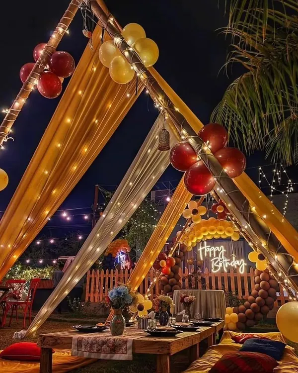 A stunning outdoor gazebo party at night, with yellow and white drapes, fairy lights, and a low-seating arrangement for a magical birthday dinner.