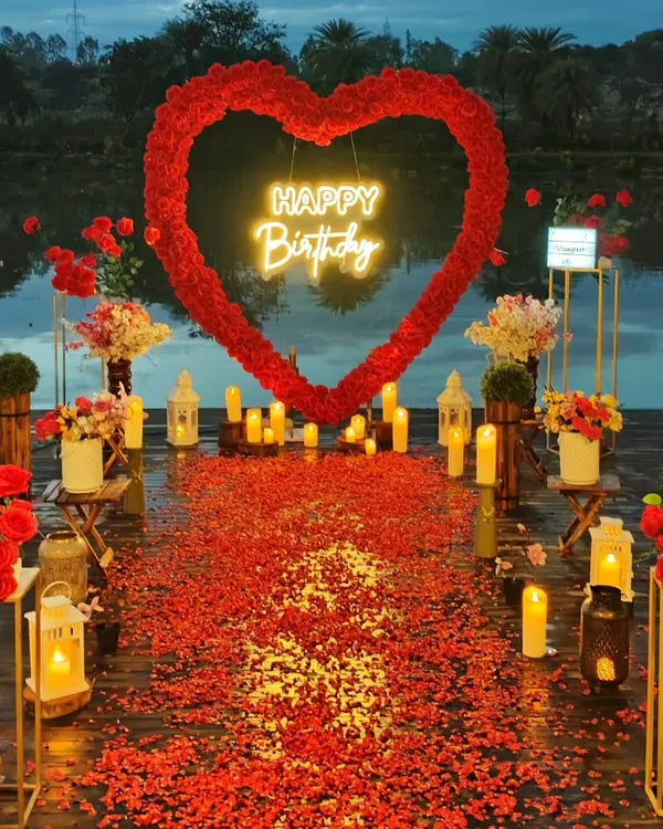 This stunning lakeside setup is perfect for a romantic birthday surprise or an intimate anniversary. The oversized red rose heart, glowing neon sign, and pathway of petals and candles create an unforgettable, picture-perfect moment.