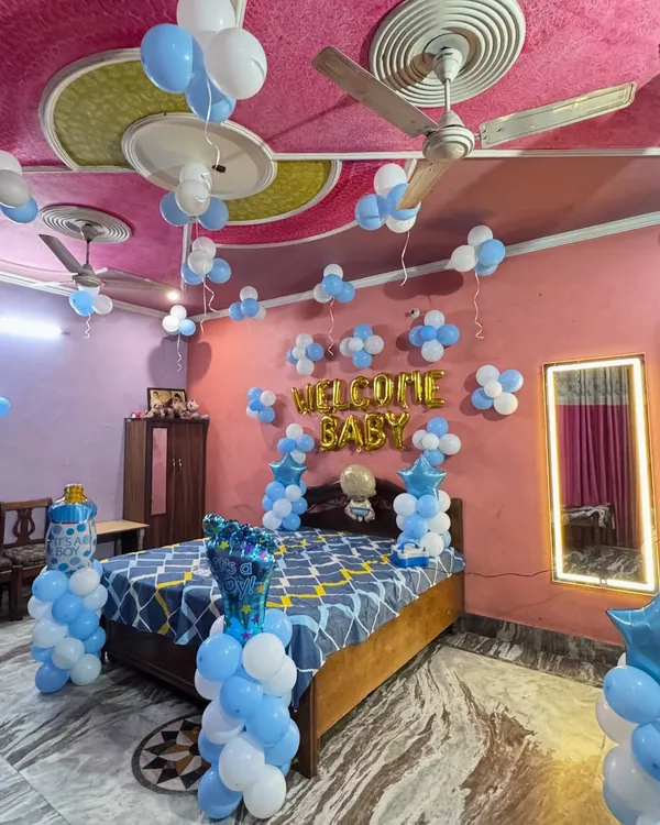 A classic 'Welcome Baby' room decoration for a baby boy. The setup includes blue and white balloons on the ceiling and walls, with foil balloons spelling out 'WELCOME BABY' over the bed.