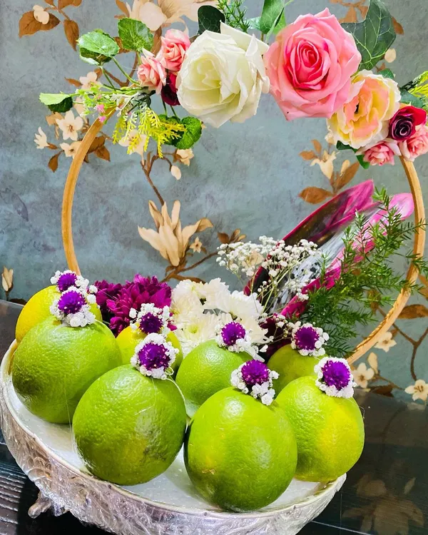 An elegant fruit platter featuring fresh limes and a beautiful floral arrangement. I use ornate silver and gold-rimmed baskets that you can rent for displaying fruits and other offerings.