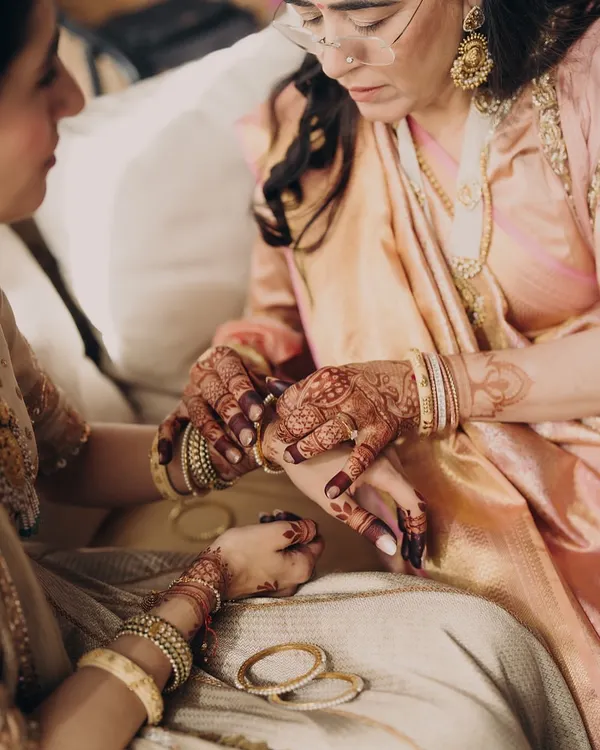 The mothers have seen it all. We celebrate the OG icons, styling them in quiet luxury that reflects their grace and wisdom. Here, a mother helps her daughter with her bangles, a timeless moment of connection.