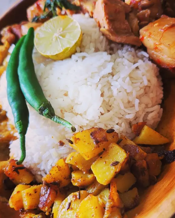 A hearty Naga meal plate centered around my signature Pork with Axone (fermented soybean). The plate also includes steamed rice, aloo fry, and a simple taro root curry, garnished with fresh green chili and lemon.