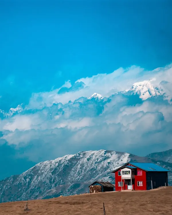 A lone house stands against the backdrop of the mighty Kanchenjunga range. This is a typical, stunning view you'll encounter on the Sandakphu trek, where we stay in cozy tea houses along the India Nepal border.